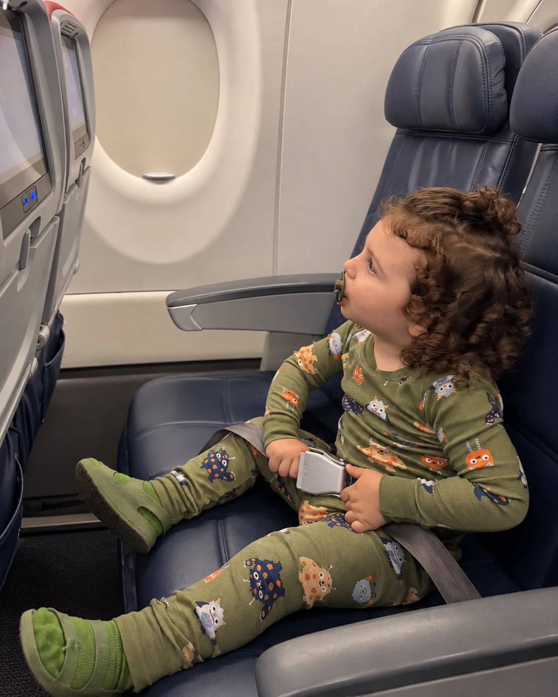Gavi in an airplane seat, holding the buckle of his seatbelt